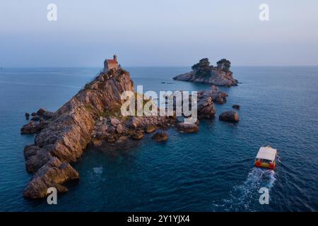 Luftaufnahme Sveta Nedjelja Insel mit magestischer kleiner Kirche auf der Klippe während der Abendstunden Sonnenuntergang mit Touristenboot, Balkanreisen, lan Stockfoto