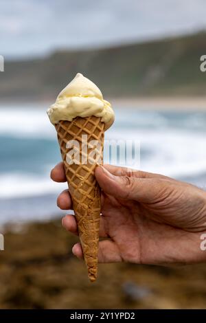 Eine Nahaufnahme eines Vanilleeises, das gehalten wird, mit dem unfokussierten Ozean dahinter Stockfoto