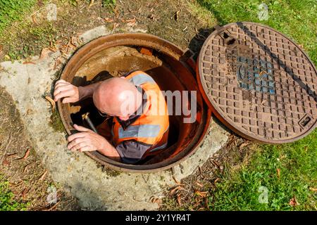 UN ouvrier enlève la plaque d'égoût pour détecter les fuites d'eau dans les canalisations de Distribution. IL Pose des Instruments de mesurent fähig Stockfoto