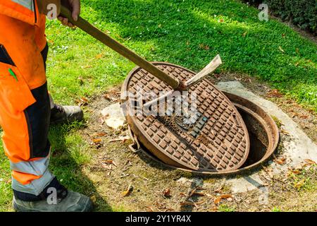 UN ouvrier enlève la plaque d'égoût pour détecter les fuites d'eau dans les canalisations de Distribution. IL Pose des Instruments de mesurent fähig Stockfoto