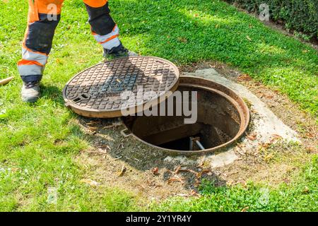 UN ouvrier enlève la plaque d'égoût pour détecter les fuites d'eau dans les canalisations de Distribution. IL Pose des Instruments de mesurent fähig Stockfoto