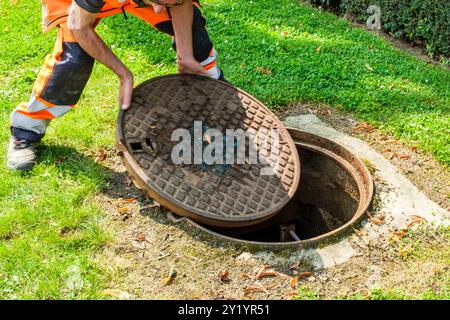 UN ouvrier enlève la plaque d'égoût pour détecter les fuites d'eau dans les canalisations de Distribution. IL Pose des Instruments de mesurent fähig Stockfoto