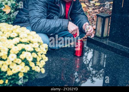 Hände von Menschen zünden Kerzen auf Gräbern, dekoriert mit Laternen, brennenden Kerzen, bunten Chrysanthemen Blumen, katholischen Symbolen Stockfoto