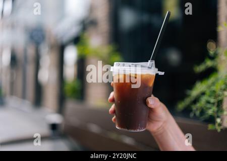 Beschnittene Aufnahme einer nicht erkennbaren Frau, die draußen einen Plastikbecher zum Mitnehmen mit Eisgetränk hält. Großaufnahmetasse kalten Bubble-Tee mit Strohhalm bei Weibchen Stockfoto