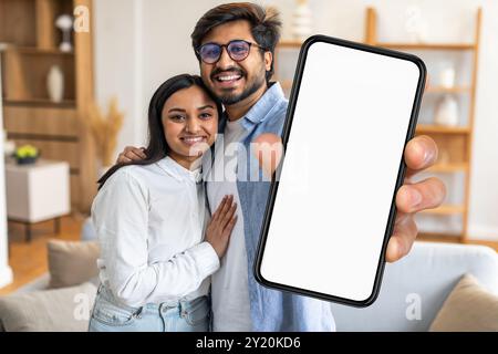 Glückliches Paar posiert zuhause zusammen und hält ein leeres Smartphone drinnen Stockfoto