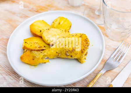 Gebratenes Hähnchen am Schenkel mit Knoblauch in eigenem Saft gewürzt und garniert mit Stücken gebackener Kartoffeln Stockfoto