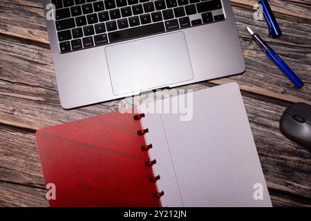 Ein flaches Design mit rotem Notizbuch, Füllfederhalter, Laptop und Maus auf einem rustikalen Holzschreibtisch, das moderne Grundausstattung für den Arbeitsplatz darstellt Stockfoto