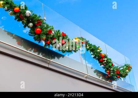 Der Weihnachtskranz hängt von einem Balkon. Der Kranz besteht aus grünen und roten Blättern und ist mit kleinen, bunten Kugeln bedeckt. Die Szene ist hell und Stockfoto
