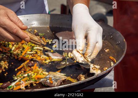 Koch grillt frischen Fisch, kocht beim Food Festival im Freien, Hände in Handschuhen, Street Food, kulinarisches Event-Konzept Stockfoto