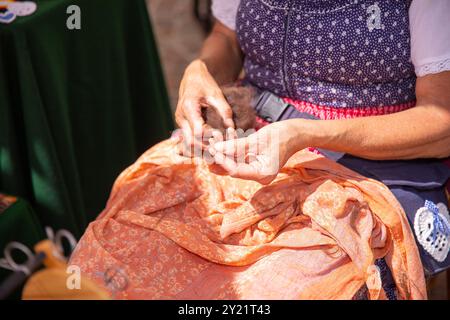 Nahaufnahme einer älteren Frau in traditioneller Tracht, die während einer Veranstaltung im Freien von Hand Wolle spinnt, Kulturerbe-Konzept Stockfoto