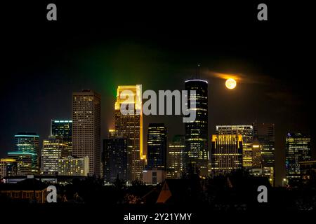 Havest Moon, der nachts über Downtown Minneapolis, Minnesota, aufsteigt und die wunderschöne Skyline der Stadt mit hellen Lichtern beleuchtet Stockfoto