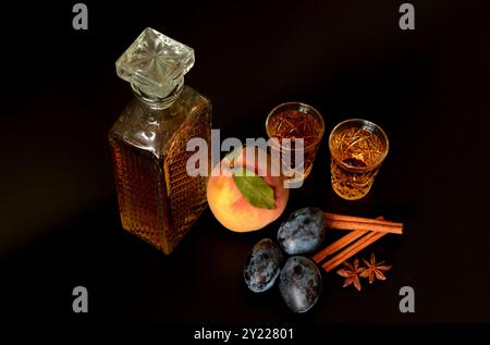 Pfirsichlikör mit Zimt und Anis auf schwarzem Hintergrund, starker hausgemachter Alkohol in Kristallgläsern, reife Früchte und Gewürze. Nahaufnahme. Stockfoto