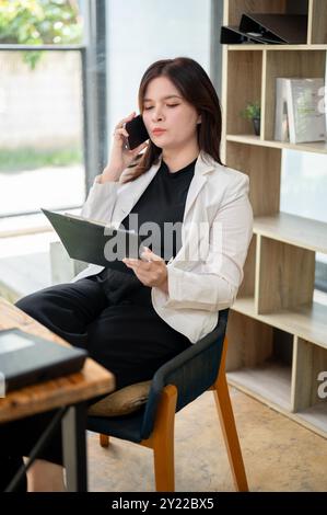 Eine professionelle kaukasische Geschäftsfrau oder Managerin liest Dokumente, während sie mit einer Klientin telefoniert, während sie bei ihr sitzt Stockfoto