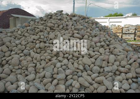 Weite Sicht auf einen großen Steinhaufen bis zum blauen Himmel und weißen Wolken im Rücken. Gekrümmter Steinhaufen, alte Baumaterialien und Gebäude hinten. N Stockfoto