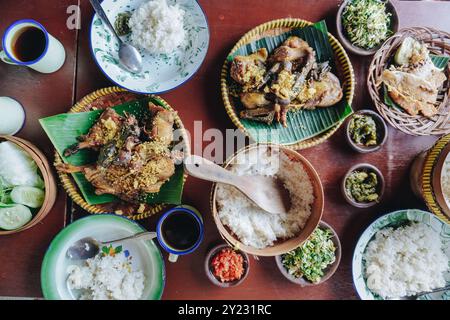 Ein Tisch mit verschiedenen asiatischen Speisen, einschließlich Reis, Fleisch und Gemüse, mit Tellern, Schüsseln und Utensilien. Stockfoto