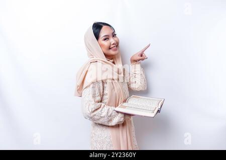 Junge asiatische Muslime lächelnd, während sie auf Platz neben ihr zeigen und den Koran halten. Stockfoto