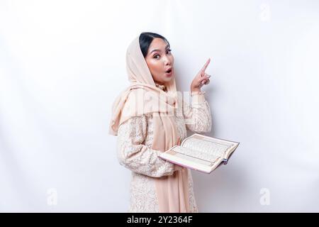 Schockierte junge asiatische Muslime, während sie darauf hinwies, Platz neben ihr zu kopieren und den Koran zu halten. Stockfoto