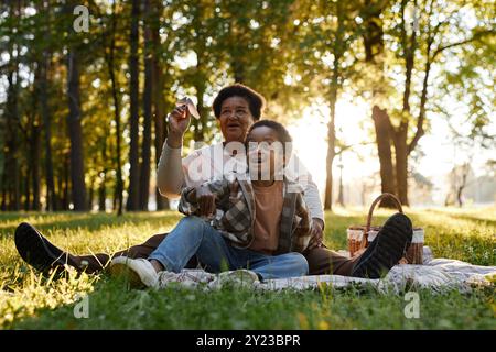 Afroamerikanische Großmutter und Enkel spielen mit Papierflugzeugen beim Picknick im örtlichen Park Stockfoto
