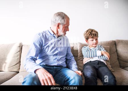 Opa streitet mit seinem Enkel. Ein wütender Junge sitzt auf dem Sofa und widerspricht seinem Großvater. Stockfoto
