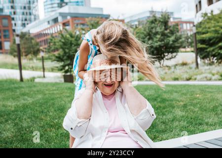 Mädchen, das Großmutters Augen mit Händen bedeckt. Enkelin verbringt Zeit mit der älteren Großmutter, in den Sommerferien, nach der Schule. Stockfoto