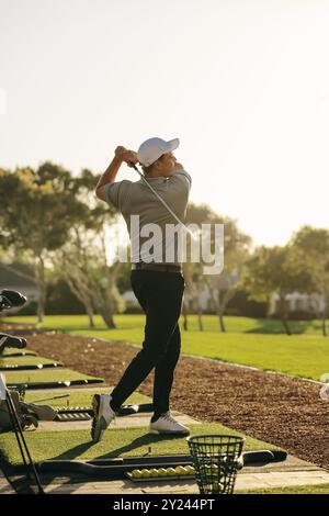 Profi-Golfspieler, die ihre Technik bei einer Driving Range Session am frühen Morgen bei Sonnenaufgang verfeinern. Golfspieler üben seinen Schwung. Stockfoto