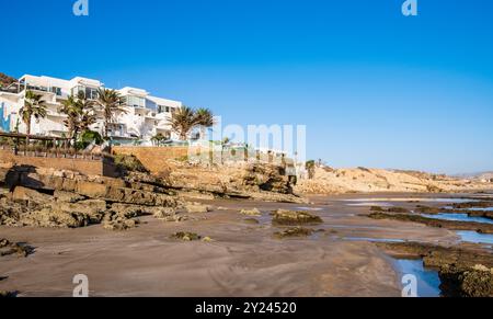 Hotelkomplex auf einer Klippe am Strand La Source in Taghazout in der Nähe von Agadir, Marokko. Die zerklüftete felsige Küste des Atlantiks zieht Surfer und Touristen an Stockfoto