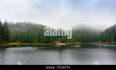 Herrlicher Bergsee im Herbstnebel. Schöne Naturlandschaft mit Nadelwald. Die Oberfläche des Wassers spiegelt die Schönheit der exquisiten Landschaft wider Stockfoto