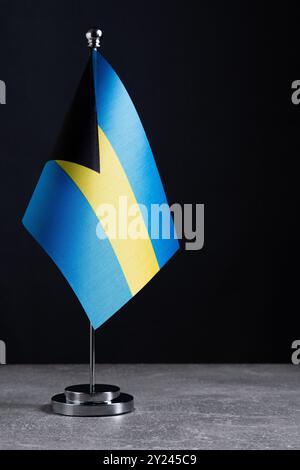Bahamas-Flagge auf Metallständer auf grauem Tisch vor schwarzem Hintergrund Stockfoto
