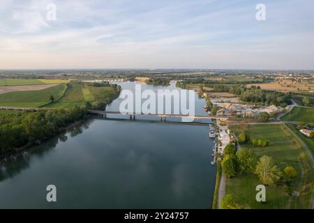 Aus der Vogelperspektive auf eine Brücke über einen ruhigen Fluss, umgeben von grünen Feldern unter einem blauen Himmel mit Wolken, die sich im Wasser spiegeln Stockfoto