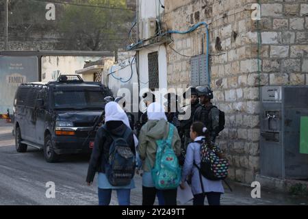 Nablus, Palästina. 28. November 2021. Palästinensische Schulkinder laufen auf dem Weg zur Schule unter dem wachsamen Auge israelischer Soldaten im Dorf Lubban Ash-Sharqiya südlich von Nablus. Das Dorf und die Schulen wurden kürzlich täglich von jüdisch-israelischen Siedlern angegriffen, die auch versucht haben, den Zugang der Schüler zur Schule zu behindern. Die Bewohner haben Proteste gegen die Gewalt der Siedler organisiert, wobei israelische Truppen die Demonstrationen unterdrücken und einige ihrer Teilnehmer verhaften Stockfoto