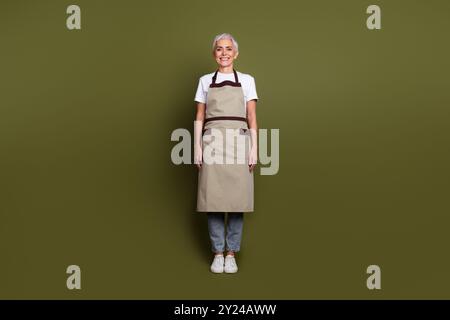 Foto in voller Länge von glänzender attraktiver Dame gekleidete Schürze, die Getränke zubereitet lächelnder leerer Raum isolierter grüner Hintergrund Stockfoto