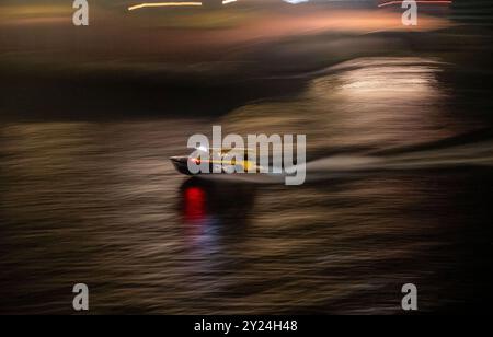 Wassertaxi fährt nachts durch den Flusshafen der Stadt, Hochgeschwindigkeits-Weichzeichner-Schwenk Stockfoto