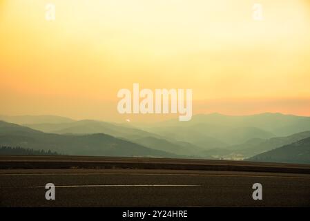 Sonnenuntergang durch Wildfeuer-Rauch über überlagerten Bergen. Stockfoto