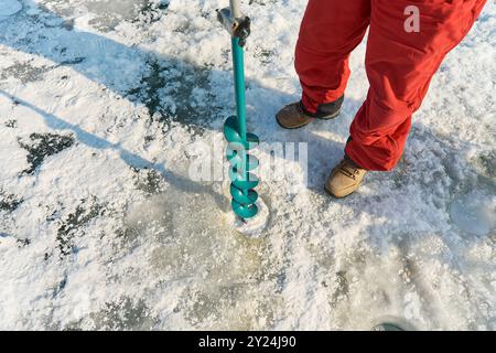 Ein warm gekleideter Asiate bohrt im Winter ein Loch ins Eis Stockfoto