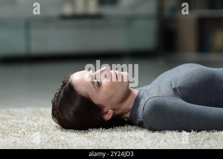 Traurige Frau beschwert sich mit verlorenem Blick, der zu Hause auf einem Teppich liegt Stockfoto