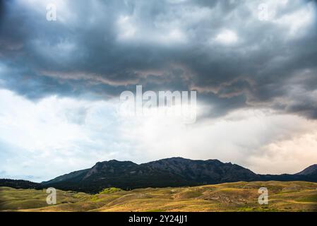 Dunkle, dramatische Wolken sammeln sich über sanften Hügeln und fernen Bergen. Stockfoto