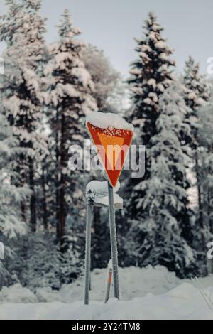 Schneebedecktes gelbes Straßenschild vor Bäumen im Winter in Rovaniemi, Lappland Stockfoto