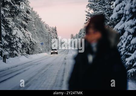 Das Mädchen stand auf einer verschneiten Straße mit Autos, die im Winter in Rovaniemi, Lappland, vorbeifuhren Stockfoto