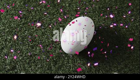 Bild von Konfetti über weißem Rugbyball auf Gras Stockfoto