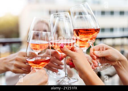 Nahaufnahme viele weibliche Frauenhände halten klirrende Rosenweingläser feiern Toast Party Terrasse warmer Sonnenuntergang Sonne Hintergrund. Freundin genießt einen Drink Stockfoto