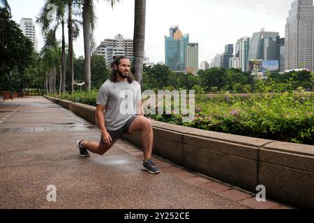 Mann, der sich nach einem Lauf im Benchakitti Park in Bangkok, Thailand, ausdehnt Stockfoto