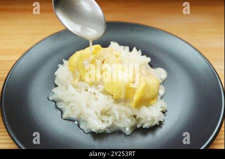 Mit einem Löffel gekochte Kokosmilch mit Durianfleisch zu Kao Niaow Turian (thailändischer Sticky Reis mit Durian) hinzufügen Stockfoto