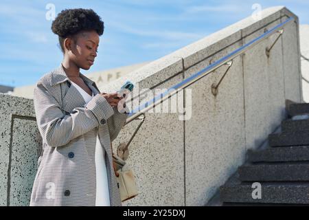 Junge Frau, die das Telefon auf einer städtischen Treppe im Freien benutzt Stockfoto