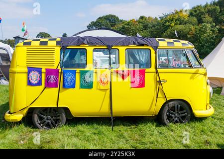 Knallgelber VW Volkswagen Typ 1 bulli Vintage-Wohnmobil auf Gras geparkt mit farbenfrohen Gobelfahnen bei einem Outdoor-Festival Stockfoto