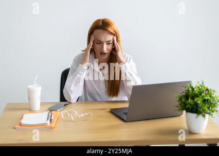 Besorgte, ermüdete Geschäftsfrau mit Brille und Kopfschmerzen bei der Arbeit. Stockfoto