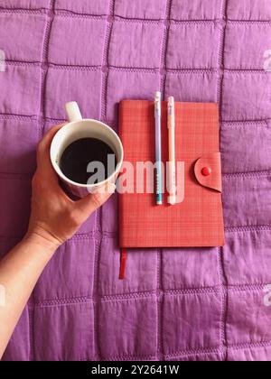 Notizbuch, Stifte und Kaffee in lebendigem Öko-Leder auf einer lila Decke Stockfoto