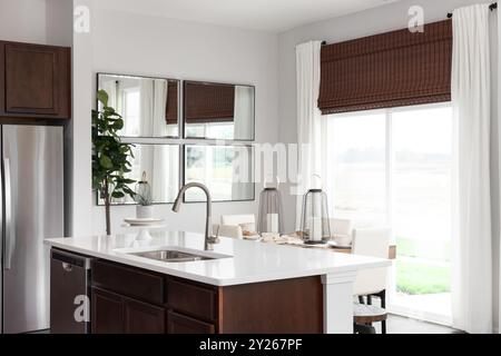 Ein Küchendetail mit einer Holzinsel und einer Arbeitsfläche aus weißem Marmor mit Blick auf ein Esszimmer vor einer hellen Schiebetür. Stockfoto