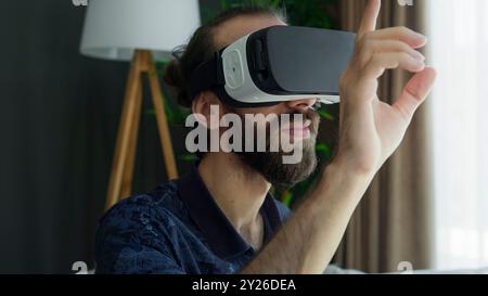 Ein Mann, der ein VR-Headset trägt, interagiert mit einer Virtual-Reality-Umgebung und streckt mit der Hand aus, während er durch die immersive Erfahrung navigiert Stockfoto