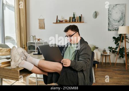 Ein Mann mit Down-Syndrom sitzt bequem zu Hause und konzentriert sich auf seinen Laptop. Stockfoto