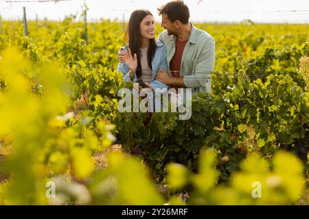 Unter der warmen Nachmittagssonne schlendern ein Paar durch einen Weinberg und teilen sich freudig einen Moment, während sie gemeinsam einen Haufen frisch geernteter Trauben bewundern Stockfoto